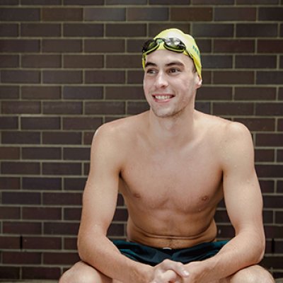 Thomas Neilll sitting with arms on his knees wearing his swimming cap and goggles 